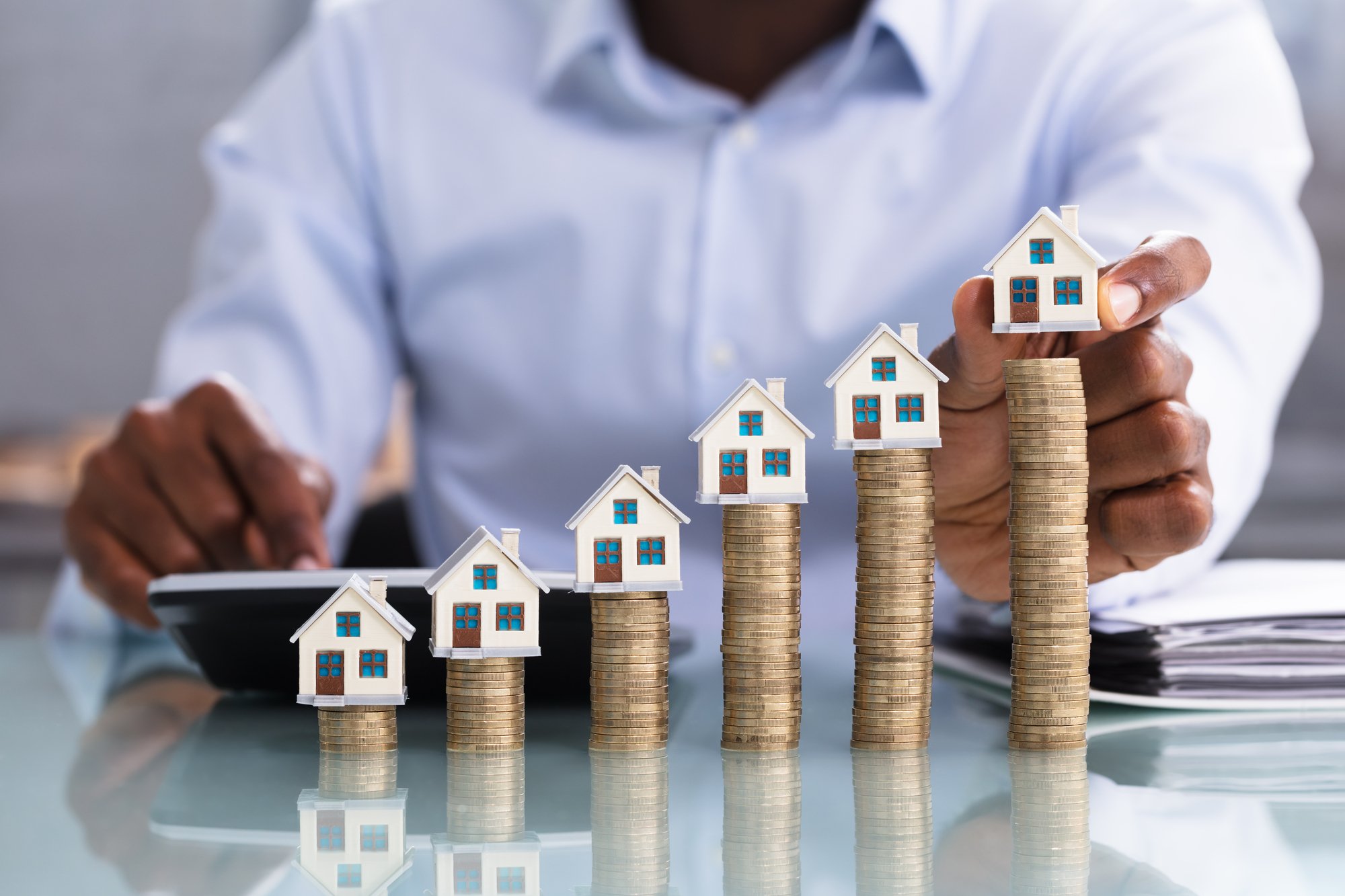 Close-up Of A Business Person Placing Miniature House Model On Stacked Coins