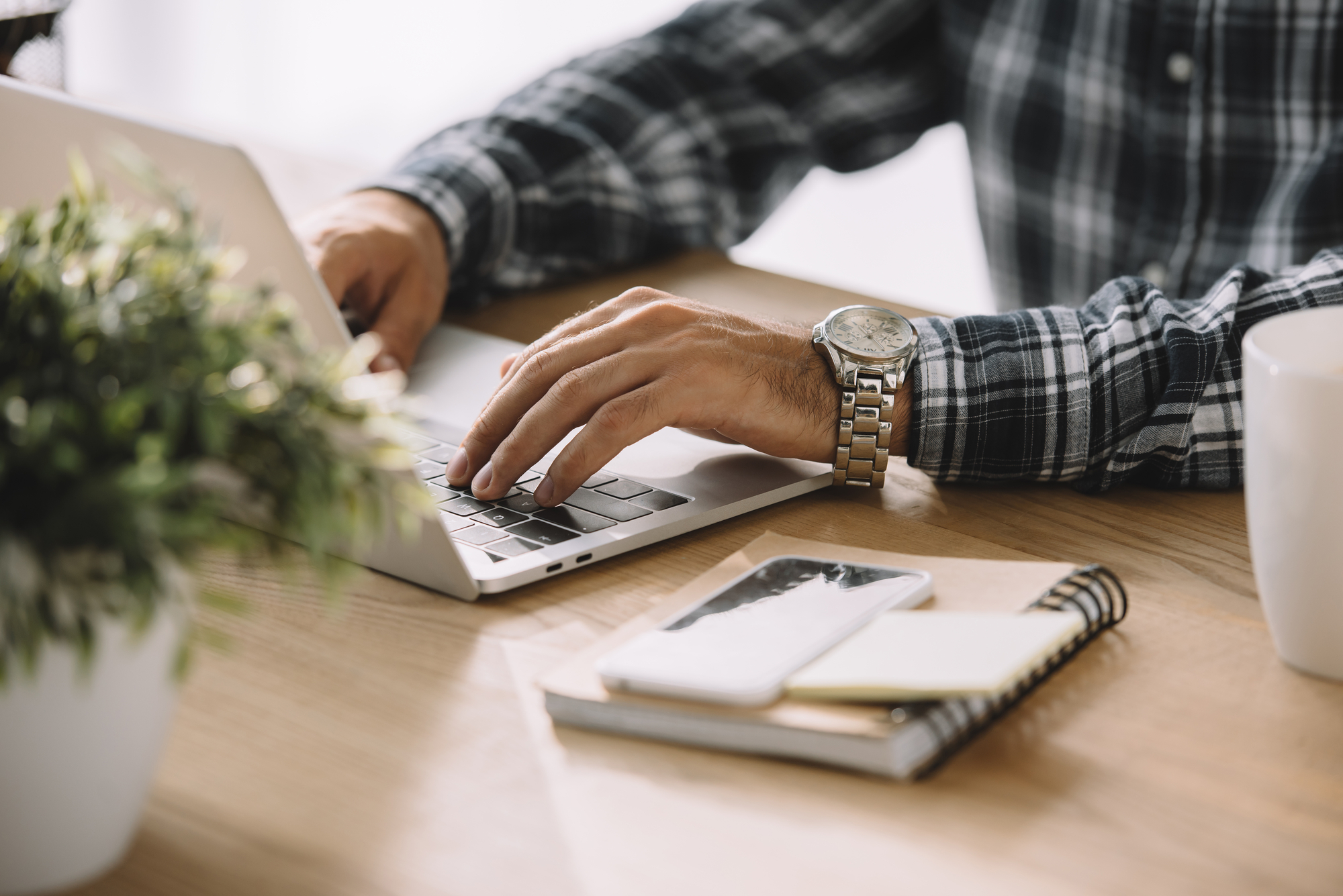 Cropped shot of man in plaid shirt using laptop at workplace